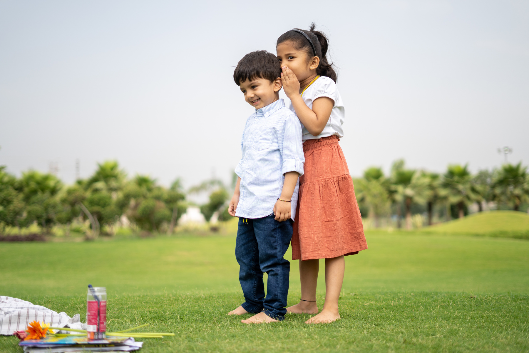 Girl Whispering on Little Boy's Ear Outdoors